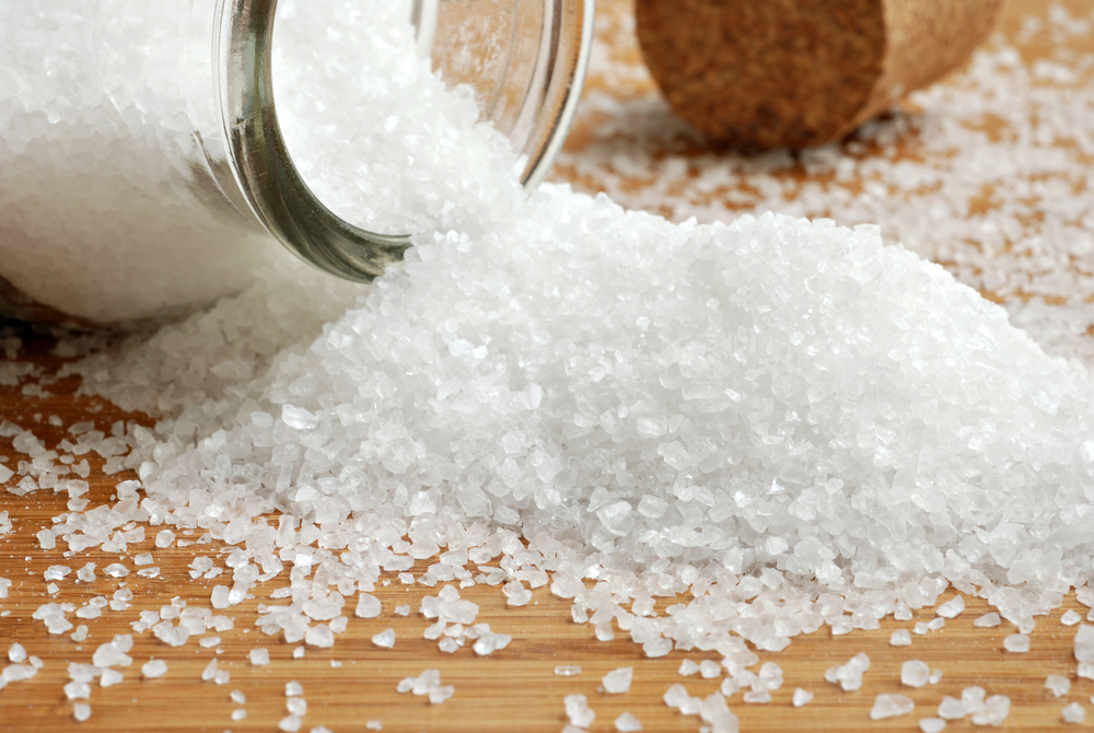 Sea salt spilling from glass bottle onto bamboo surface. Cork bottle stopper in background. Macro with shallow dof.